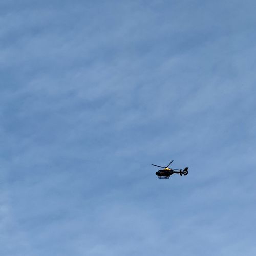 A police helicopter hovering against a blue sky mottled by wispy clouds.